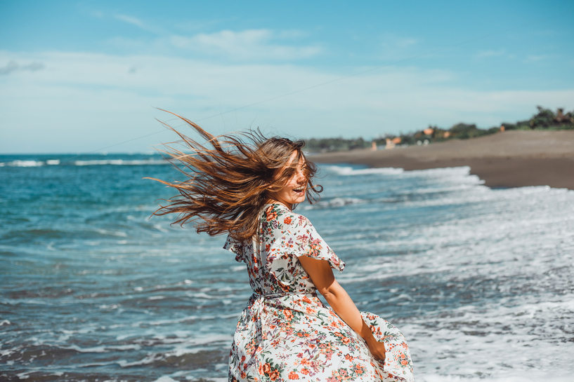 mulher a sorrir com os cabelos ao vento na praia